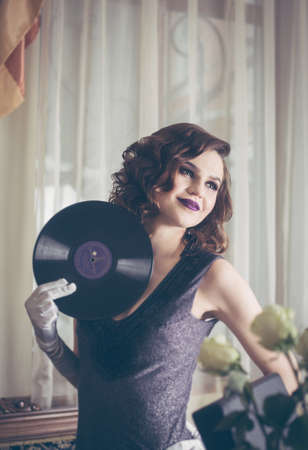 Young beautiful woman in retro style, with a vinyl record. Vintage interior. Studio photo.の写真素材