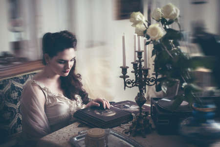 Young woman looks at a photo album. Vintage old style, retro interior.の写真素材