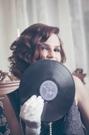 Young beautiful woman in retro style, with a vinyl record. Vintage interior. Studio photo.の写真素材
