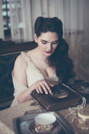 Young woman looks at a photo album. Vintage style, retro interior.の写真素材