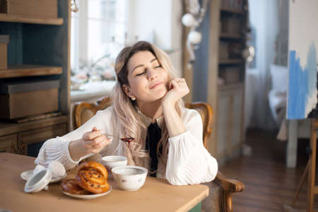 A young woman has breakfast with tea and pastries with jam.の写真素材