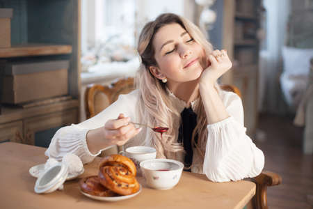 A young woman has breakfast with tea and pastries with jam.の写真素材