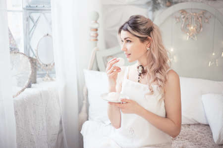 Cute young woman eating sweets in the morning in the bedroom. Gentle winter morning.の写真素材
