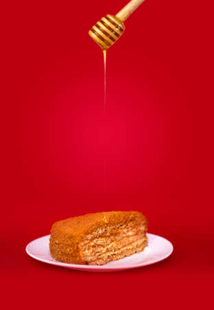 Honey cake in a plate on a red background with pouring honey. Studio shooting.の写真素材