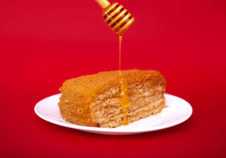Honey cake in a plate on a red background with pouring honey. Studio shooting.の写真素材