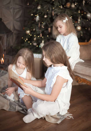 Sister girls are reading a book in the childrens room. Christmas and winter holidays.の写真素材