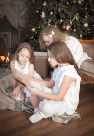 Sister girls are reading a book in the childrens room. Christmas and winter holidays.の写真素材