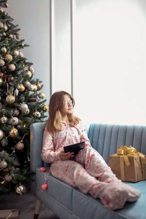 Teenager girl with a tablet near a New Year tree or in a Christmas interior.の写真素材