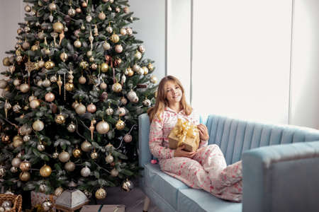 Teenager girl with a gift near a New Year tree or in a Christmas interior.の写真素材