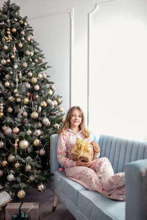 Teenager girl with a gift near a New Year tree or in a Christmas interior.の写真素材