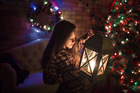 A girl near a Christmas tree with a decorative lantern in her hands, New Year and Christmas. Winter holidays.の写真素材