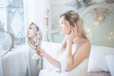 Young beautiful woman looks in the mirror in her bedroom. Morning of the bride.の写真素材