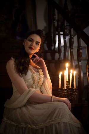 Woman in a vintage dress in the interior with candles. Retro style or theater.の写真素材