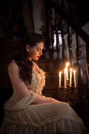 Woman in a vintage dress in the interior with candles. Retro style or theater.の写真素材