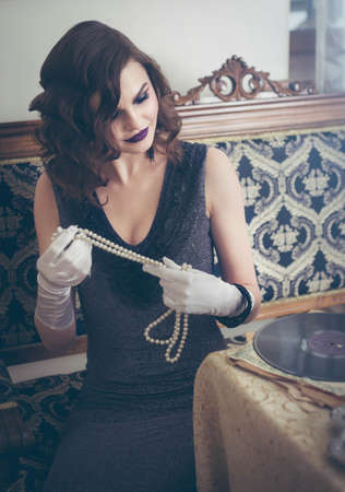 Portrait of a woman in a retro style with a necklace in her hands.の写真素材
