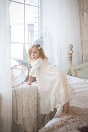 LiLittle cute girl near the window in her bedroom. Winter holidays, vintage style. Christmas and New Year.の写真素材