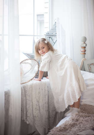 LiLittle cute girl near the window in her bedroom. Winter holidays, vintage style. Christmas and New Year.の写真素材