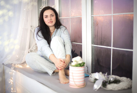 Young beautiful woman in pajamas with flowers near the window. Winter holidays.の写真素材