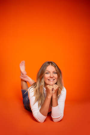 Young beautiful woman in longsleeve or crop top and jeans in the studio on an orange background. Positive emotions. High quality photoの写真素材
