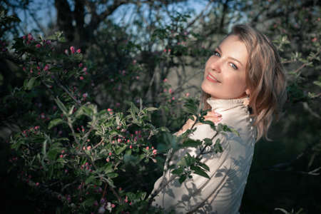 Beautiful woman in the garden among blooming apple trees in a vintage dress. Spring or summer, sunny day.の写真素材