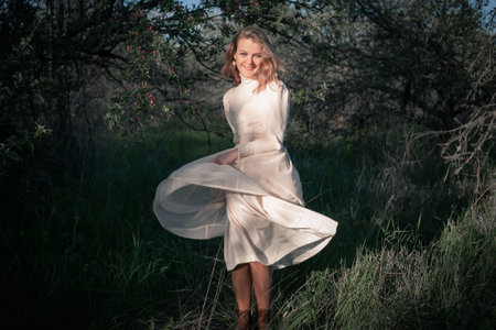 Beautiful woman in the garden among blooming apple trees in a vintage dress. Spring or summer, sunny day.の写真素材