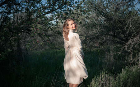 Beautiful woman in the garden among blooming apple trees in a vintage dress. Spring or summer, sunny day.の写真素材