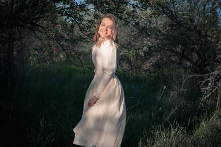 Beautiful woman in the garden among blooming apple trees in a vintage dress.の写真素材