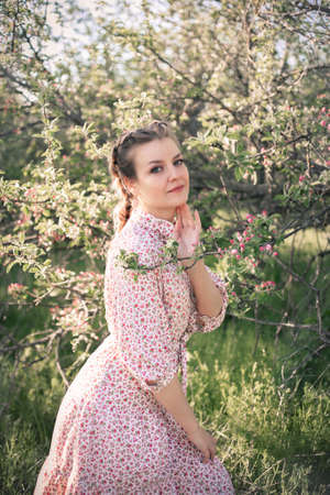 Beautiful woman in the garden among blooming apple trees in a vintage dress.の写真素材