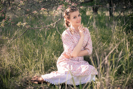 Beautiful woman in the garden among blooming apple trees in a vintage dress.の写真素材