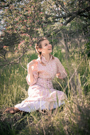 Beautiful woman in the garden among blooming apple trees in a vintage dress.の写真素材