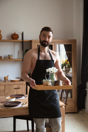 Handsome attractive man standing in kitchen with tray with flowers and coffee.の写真素材