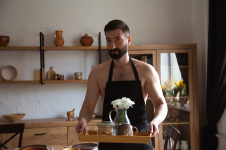 Handsome attractive man standing in kitchen with tray with flowers and coffee.の写真素材