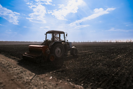 Blue tractor pulling a seed drill machine during spring sowing season.の写真素材
