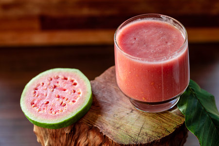 Delicious red guava juice alongside a slice of guava, in the background guavas and leaves on rustic wood.の写真素材