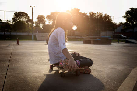 Beautiful blonde girl sitting at the table holding a skateboardの写真素材