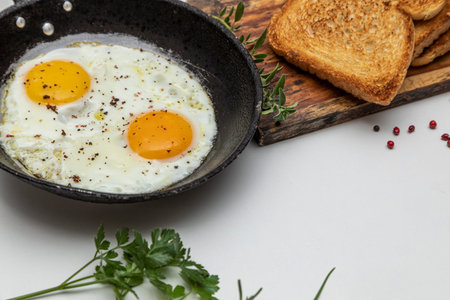 Fried eggs in a rustic iron pan, toast on a dish for breakfast.