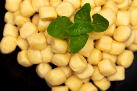 Pile of fresh raw gnocchi with basil leaves, view from above on a black dishの写真素材