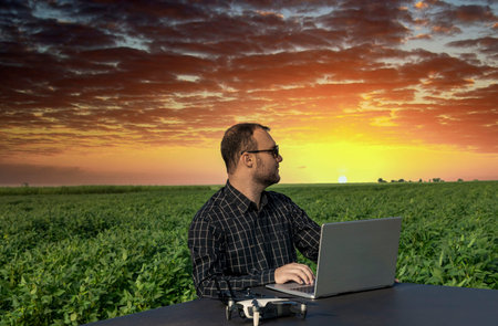 Farmer standing in soybean field looking at notebook and drone.