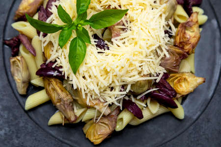 Pasta with black olives, Parmesan cheese, artichoke hearts, topped with fresh basil leaves.の写真素材