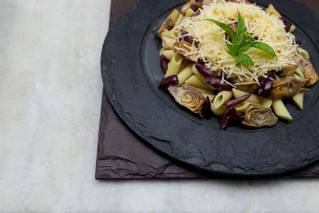 Pasta with black olives, Parmesan cheese, artichoke hearts, topped with fresh basil leaves.の写真素材