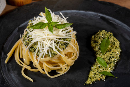 Spaghetti pasta with pesto sauce and fresh basil leaves in black stone dish on wooden background