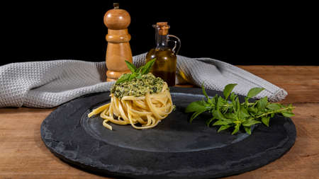 Spaghetti pasta with pesto sauce and fresh basil leaves on black plate.の写真素材