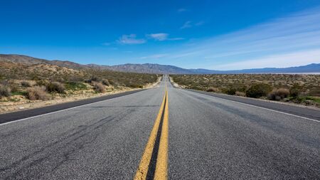 Yellow dividing strip on asphalt speedway along field and hillの写真素材
