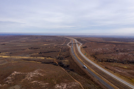 Drone view of white trucks moving fast on long highway in empty deserted lands