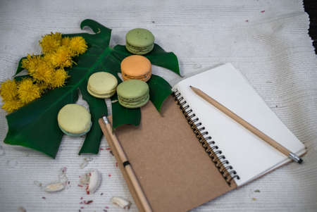 Crushed pastel, orange and green macaroons on a wood background with whole one in white plate with jug with flowers on the backの写真素材