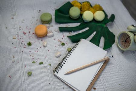 Crushed pastel, orange and green macaroons on a wood background with whole one in white plate with jug with flowers on the backの写真素材