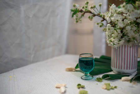 Crushed pastel, orange and green macaroons on a wood background with whole one in white plate with jug with flowers on the backの写真素材