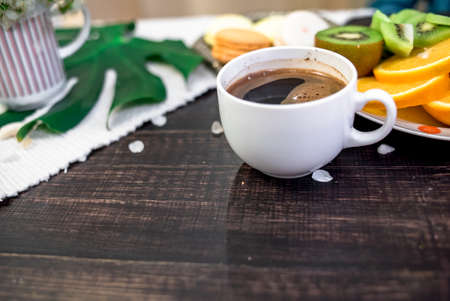 Crushed pastel, orange and green macaroons on a wood background with whole one in white plate with jug with flowers on the backの写真素材