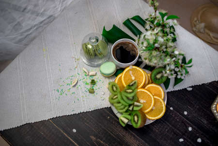 Crushed pastel, orange and green macaroons on a wood background with whole one in white plate with jug with flowers on the backの写真素材
