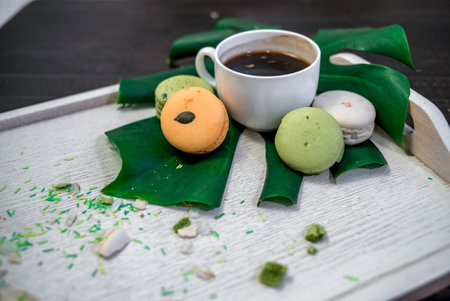 Crushed pastel, orange and green macaroons on a wood background with whole one in white plate with jug with flowers on the backの写真素材